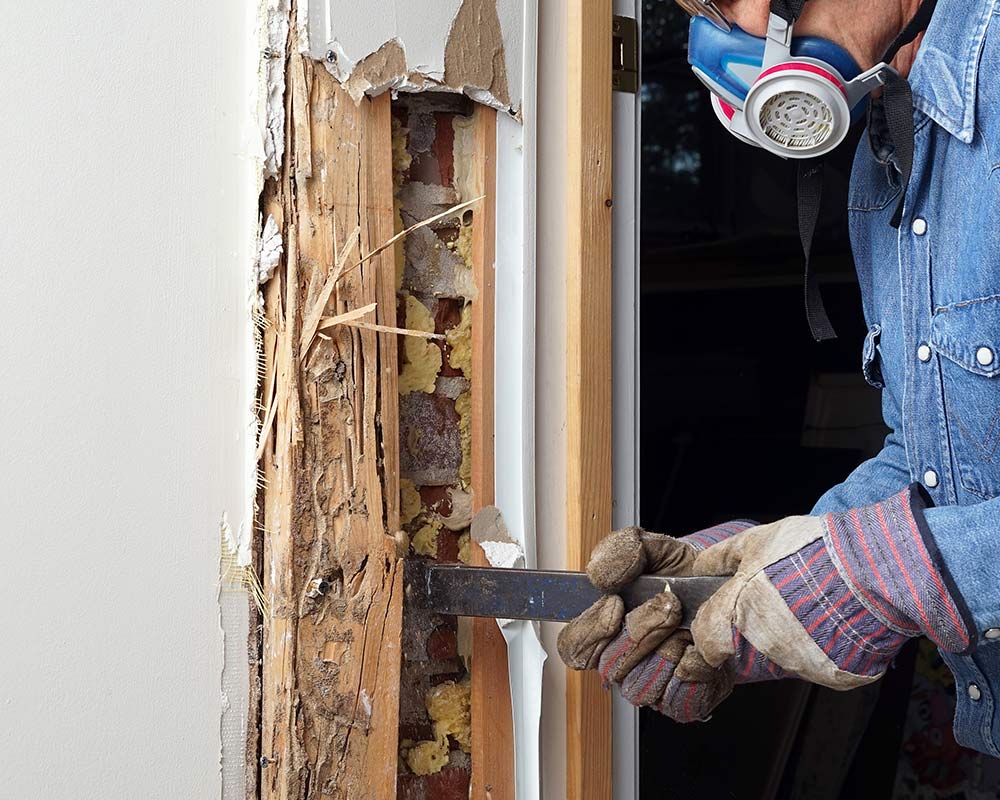 A man is holding a hammer and nails the wall.